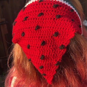 Pode incluir: Um bandana vermelho de crochê com pontos pretos, que se assemelha a uma melancia, com acabamento verde e branco.