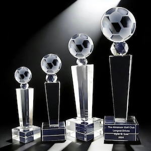 May include: Four clear crystal trophies with soccer ball toppers. The trophies vary in size, with a soccer ball design on top. The bases are engraved with text that reads "The Almansor Golf Club Longest Drives Kyle S. Lee 2024."