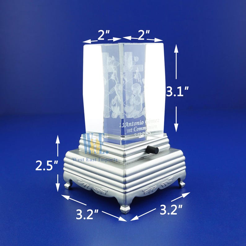 May include: A clear glass cube with a 3D engraved image of a cross and flowers. The cube is mounted on a silver metal base with a wind-up music box mechanism. The base measures 3.2 inches by 3.2 inches and is 2.5 inches tall. The cube is 2 inches by 2 inches and 3.1 inches tall.