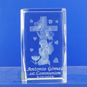 May include: A clear glass cube with an engraved image of a praying angel with wings, a cross, flowers, and hearts. The text "Antonio G&oacute;mez 1st Communion 5-13-2025" is engraved at the bottom.