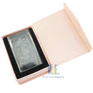 May include: A clear glass cube with an etched design of a praying angel and a cross. The cube is in a pink box with the text "Antonio Gomez 1st Communion 5-13-2025" etched on the side.