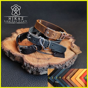 Pu&ograve; includere: Una collezione di braccialetti in pelle in vari colori, tra cui nero, marrone e grigio, con fibbie color argento. I braccialetti sono esposti su una superficie di legno, con una tabella colori di campioni di pelle nell'angolo in basso a destra. Il logo del marchio "NIKAZ Leather Craft" &egrave; visibile.