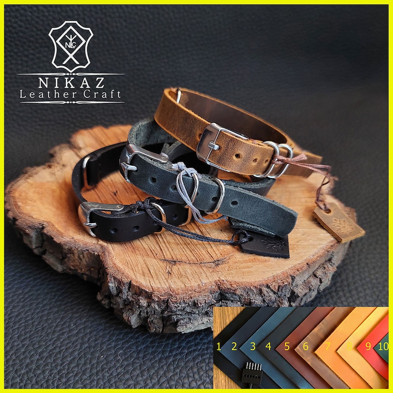 Pu&ograve; includere: Una collezione di braccialetti in pelle in vari colori, tra cui nero, marrone e grigio, con fibbie color argento. I braccialetti sono esposti su una superficie di legno, con una tabella colori di campioni di pelle nell'angolo in basso a destra. Il logo del marchio "NIKAZ Leather Craft" &egrave; visibile.