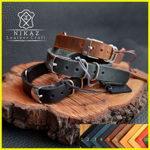 Pu&ograve; includere: Tre braccialetti in pelle marrone, nera e grigia, ciascuno con una fibbia argentata. I braccialetti sono esposti su una superficie di legno. Il logo del marchio "NIKAZ Leather Craft" &egrave; visibile in alto a sinistra.