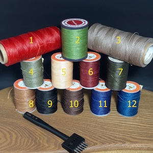 Pu&ograve; includere: Una collezione di rocchetti di filo cerato in vari colori, tra cui rosso, verde, beige e blu. &Egrave; presente anche un punzone per lavori in pelle nero. Le rocchetti sono disposti su una superficie di legno.