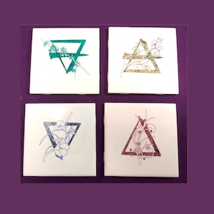May include: Four square white ceramic coasters with a triangle design and floral accents. Each coaster features a different color triangle: teal, gold, blue, and burgundy. The coasters are arranged on a purple background.