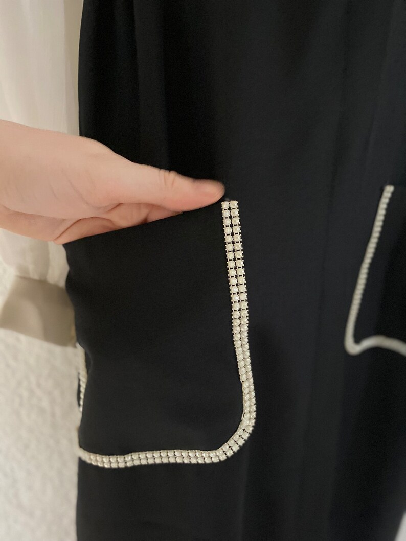May include: Black pants with a white rhinestone trim around the pockets.