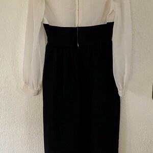 May include: A white dress with a large collar and long sleeves. The dress has a black skirt and a zipper down the back.