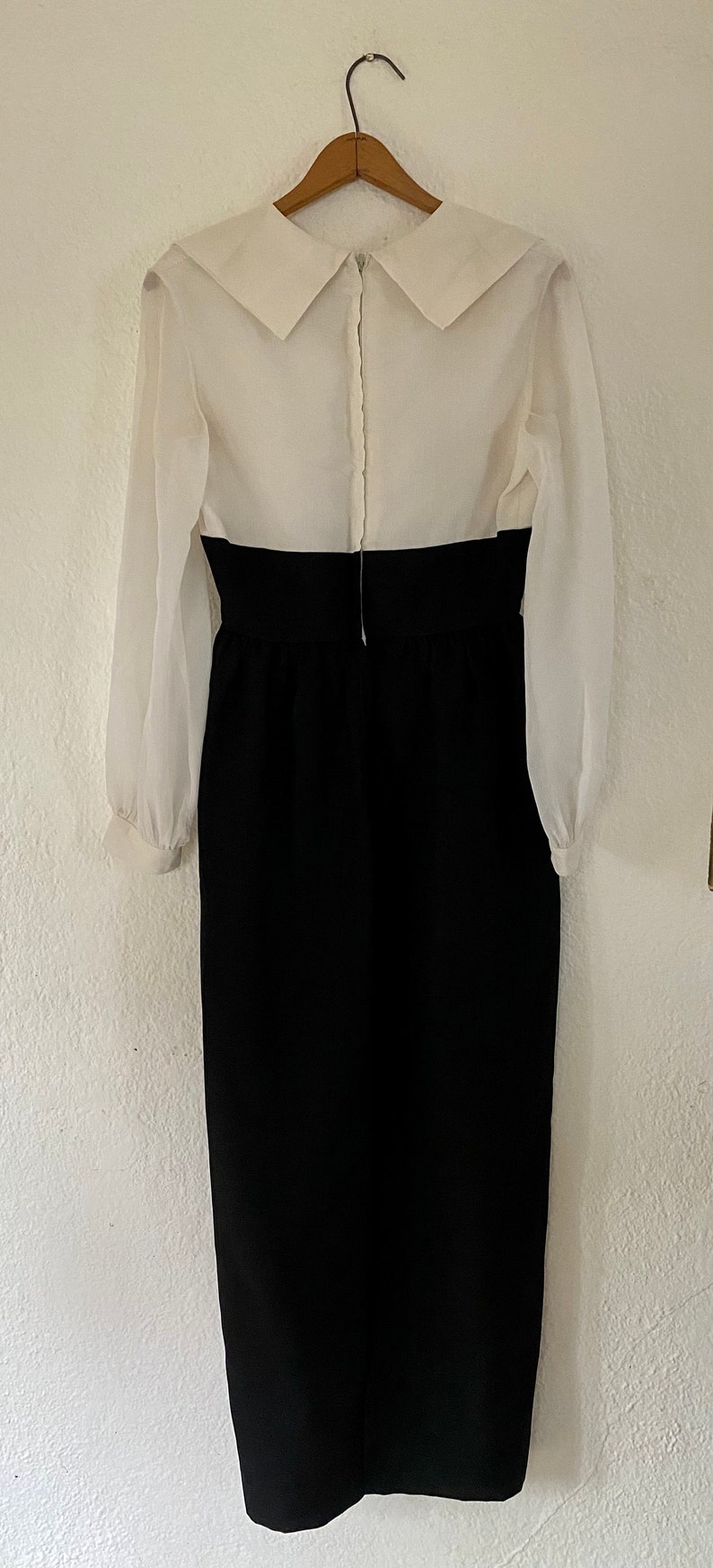May include: A white dress with a large collar and long sleeves. The dress has a black skirt and a zipper down the back.