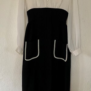 May include: A white and black dress with long sleeves and a white collar. The dress has a black skirt with two pockets trimmed with white rhinestones.