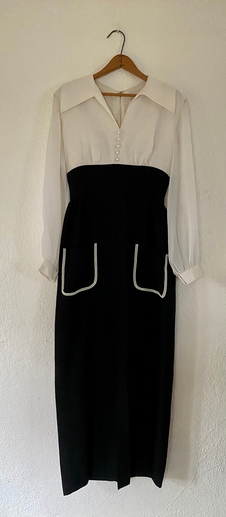 May include: A white and black dress with long sleeves and a white collar. The dress has a black skirt with two pockets trimmed with white rhinestones.