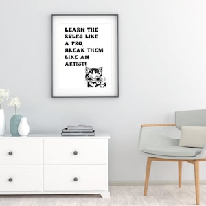 Op de afbeelding: Zwart-witte ingelijste print met een citaat dat luidt "Leer de regels als een professional. Breek ze als een kunstenaar!" en een cartoonkat met een zonnebril.
