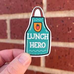 May include: A teal blue apron sticker with a red handle and a strawberry in the pocket. The text "Lunch Hero" is written in white letters on the sticker.