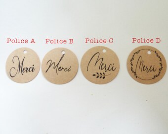 May include: Four round, kraft paper gift tags with the word "Merci" printed in black script. Each tag has a small hole at the top for stringing. The tags feature different font styles and decorative elements.