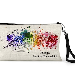 Op de afbeelding: Een witte canvas toilettas met een zwarte rits en een zwarte band. De tas heeft een kleurrijk aquarelontwerp met muzieknoten en de tekst "Linsey's Festival Survival Kit".