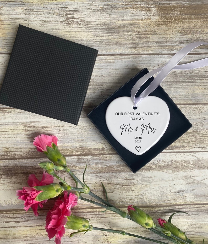 Pu&ograve; includere: Ciondolo a forma di cuore in ceramica bianca con il testo "Our first Valentine's Day as Mr & Mrs Smith 2024" in corsivo nero.