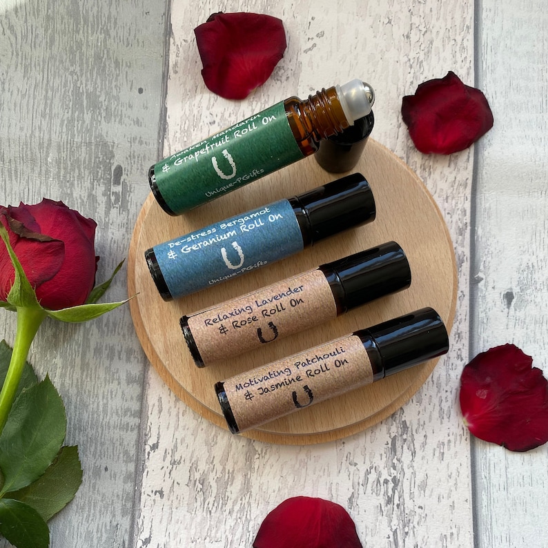 May include: Four small glass bottles with roll-on applicators, each containing a different essential oil blend. The bottles are labelled with the blend name and a horseshoe logo. The bottles are arranged on a wooden coaster with red rose petals scattered around.