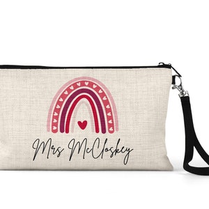 Pode incluir: Uma bolsa de maquiagem de lona bege com um z&iacute;per preto e uma al&ccedil;a preta. A bolsa apresenta um arco-&iacute;ris rosa e vermelho com cora&ccedil;&otilde;es e o texto "Mrs. Mcloskey".