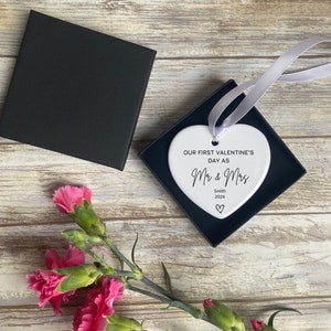Pu&ograve; includere: Ciondolo a forma di cuore in ceramica bianca con il testo "Our first Valentine's Day as Mr & Mrs Smith 2024" in corsivo nero. Il ciondolo &egrave; legato con un nastro di raso bianco ed &egrave; presentato in una scatola nera.