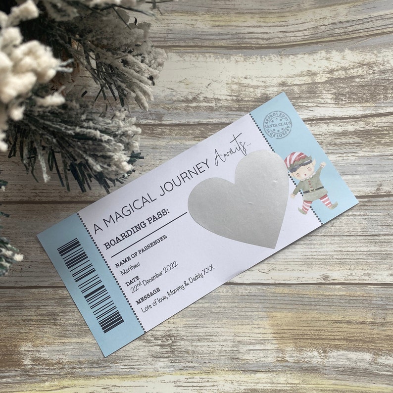 May include: A blue and white boarding pass with a silver heart-shaped scratch-off area. The pass has the text "A Magical Journey Awaits..." and "Boarding Pass:" with a space for a name, date, and message. The message reads "Lots of love, Mummy & Daddy XXX".