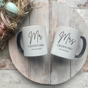 May include: Two white ceramic mugs with black handles and black text. The mug on the left says "Mr. Crawford 06.09.2024" and the mug on the right says "Mrs. Crawford 06.09.2024".