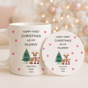 May include: A white ceramic mug and a matching round coaster, both featuring the text "HAPPY FIRST CHRISTMAS AS MY MUMMY", "Love from DAISY", and "2026". The design includes a green Christmas tree, two reindeer, and small pink stars.