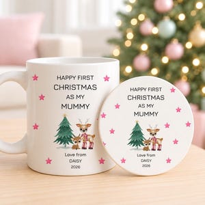 May include: A white ceramic mug and a matching round coaster, both featuring pink stars, a green Christmas tree, and two reindeer illustrations. The text reads: HAPPY FIRST CHRISTMAS AS MY MUMMY, Love from DAISY, 2026.