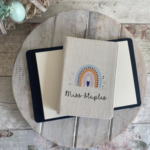 K&ouml;nnte beinhalten: Ein beigefarbener Leinen-Notizbuchumschlag mit einem Regenbogen- und Herzdesign. Der Text "Miss Staplus" ist auf dem Umschlag aufgedruckt.