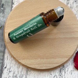 May include: A green and white label on a brown glass roll-on bottle with a silver roller ball. The label reads "Awaken Mandarin & Grapefruit Roll On".