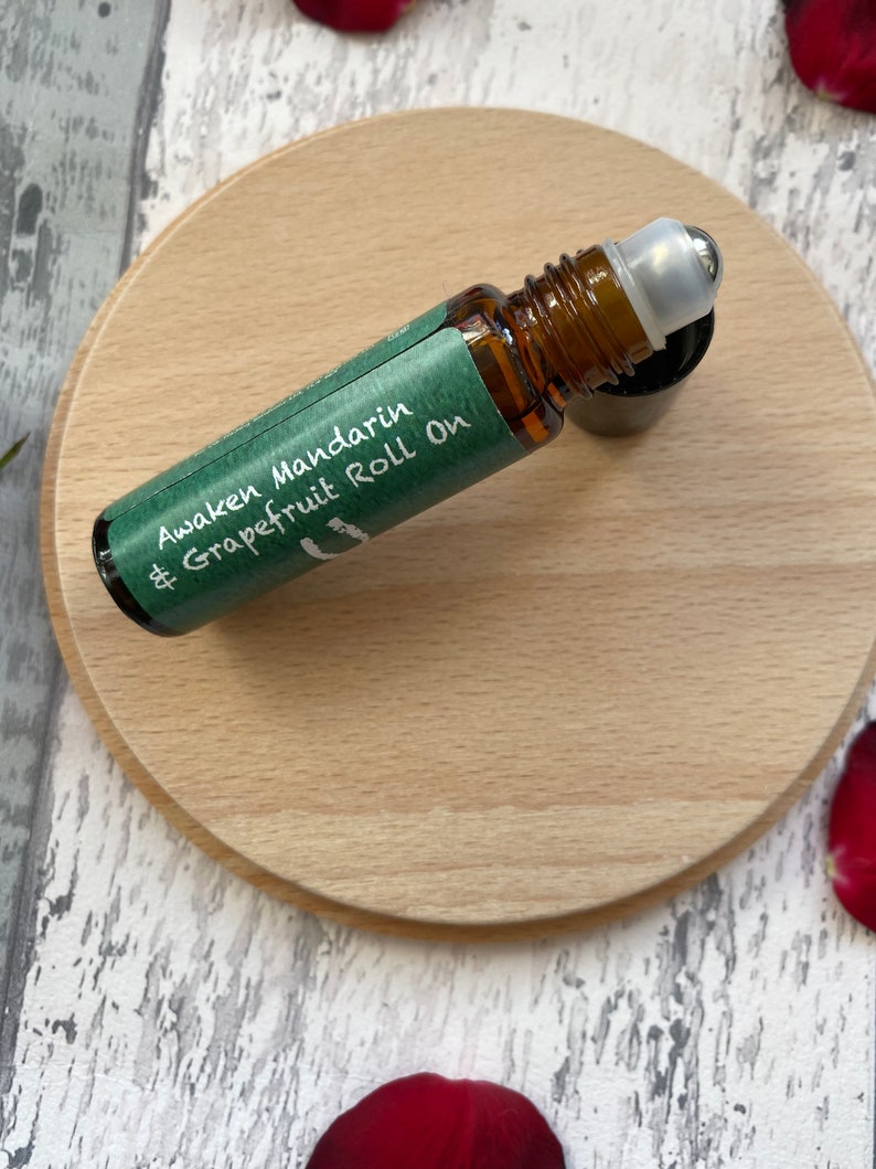 May include: A green and white label on a brown glass roll-on bottle with a silver roller ball. The label reads "Awaken Mandarin & Grapefruit Roll On".