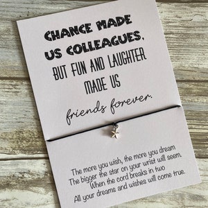May include: A white card with black text that reads "Chance made us colleagues, but fun and laughter made us friends forever."  The card is attached to a black string with a silver star charm. The text "The more you wish, the more you dream. The bigger the star on your wrist will seem. When the cord breaks in two, all your dreams and wishes will come true." is printed on the bottom of the card.