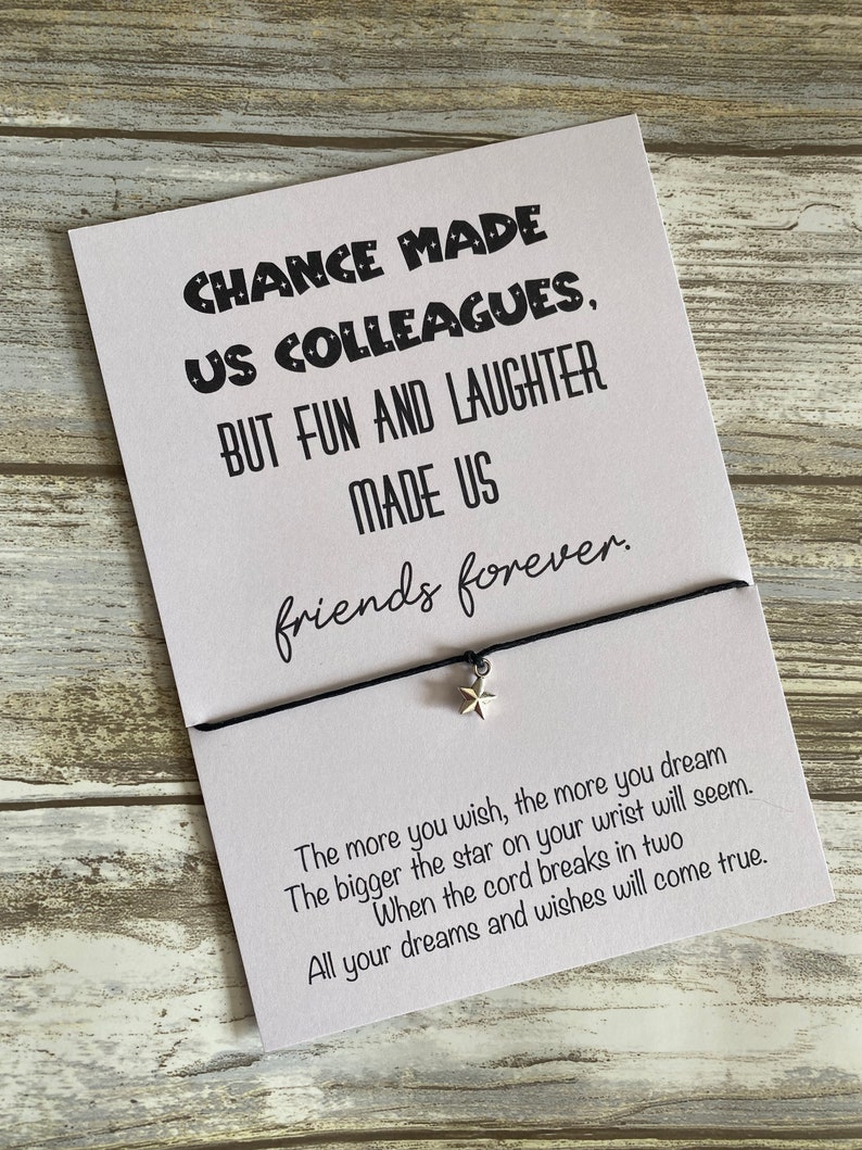 May include: A white card with black text that reads "Chance made us colleagues, but fun and laughter made us friends forever."  The card is attached to a black string with a silver star charm. The text "The more you wish, the more you dream. The bigger the star on your wrist will seem. When the cord breaks in two, all your dreams and wishes will come true." is printed on the bottom of the card.
