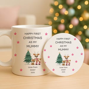 May include: A white ceramic mug and a matching round coaster, both featuring a graphic of a green Christmas tree and two deer. The text reads: HAPPY FIRST CHRISTMAS AS MY MUMMY, Love from DAISY, 2025. Pink stars are scattered across the white surface.
