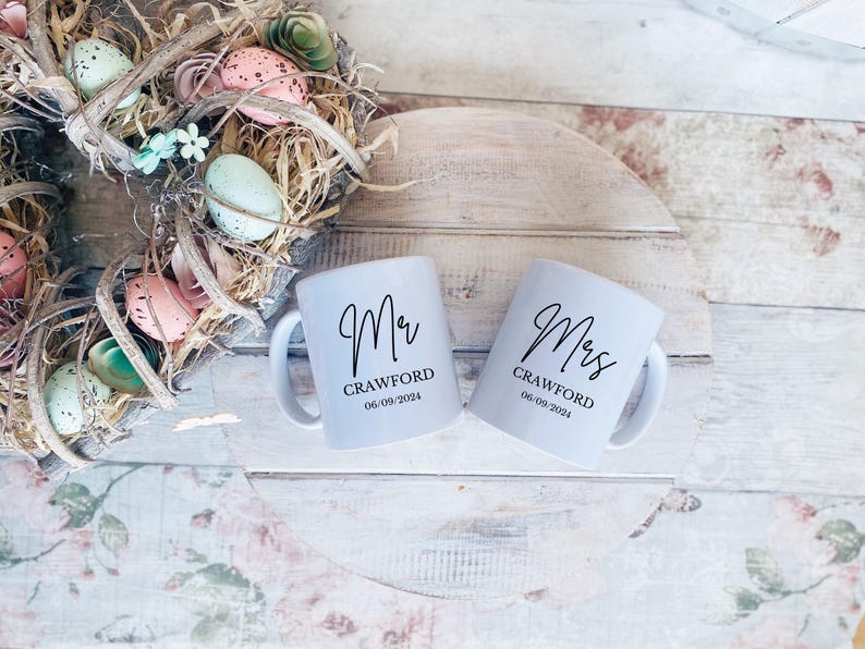 May include: Two white ceramic mugs with black lettering. The mug on the left says "Mr. Crawford 06.09.2024" and the mug on the right says "Mrs. Crawford 06.09.2024".