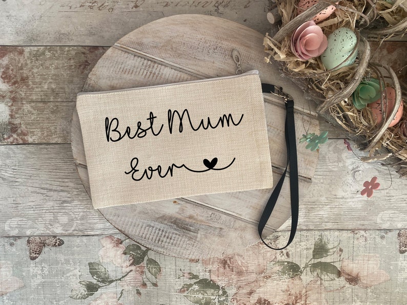 May include: A beige canvas zippered pouch with a black strap. The pouch has the text "Best Mum Ever" in black cursive lettering with a small black heart.
