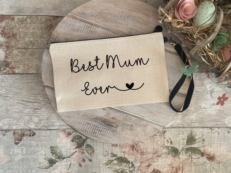 May include: A beige canvas zippered pouch with a black strap. The pouch has the text "Best Mum Ever" in black cursive lettering with a small black heart.