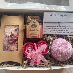 Puede incluir: Una caja de regalo llena de productos de ba&ntilde;o, incluyendo una bomba de ba&ntilde;o, sales de ba&ntilde;o y una vela de soja. La caja tambi&eacute;n incluye una tarjeta con el texto "A Birthday Wish" y una cita sobre desear una estrella.