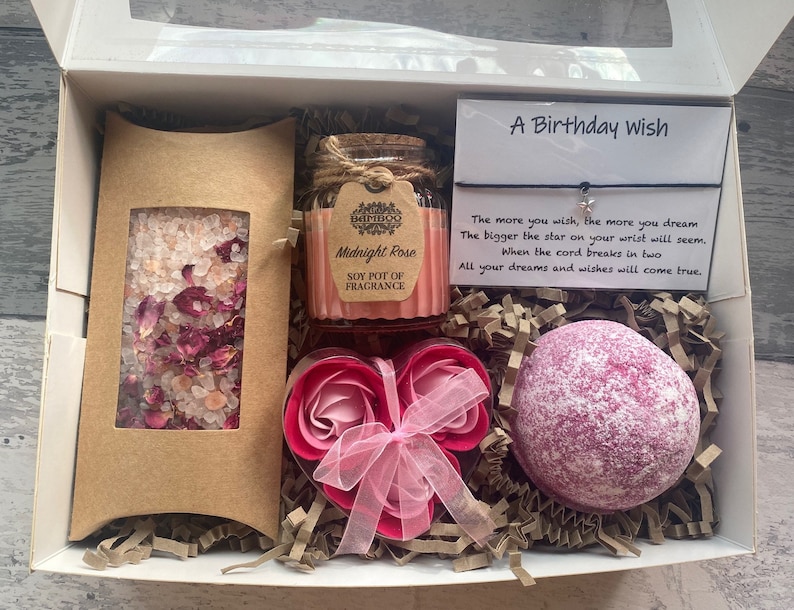 Puede incluir: Una caja de regalo llena de productos de ba&ntilde;o, incluyendo una bomba de ba&ntilde;o, sales de ba&ntilde;o y una vela de soja. La caja tambi&eacute;n incluye una tarjeta con el texto "A Birthday Wish" y una cita sobre desear una estrella.