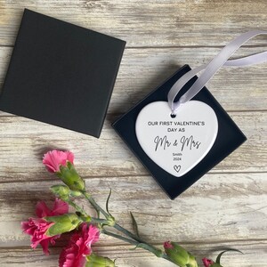 Pu&ograve; includere: Ciondolo a forma di cuore in ceramica bianca con il testo "Our first Valentine's Day as Mr & Mrs Smith 2024" in corsivo nero.