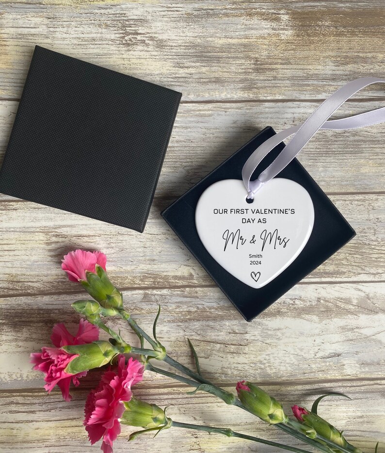 Pu&ograve; includere: Ciondolo a forma di cuore in ceramica bianca con il testo "Our first Valentine's Day as Mr & Mrs Smith 2024" in corsivo nero.