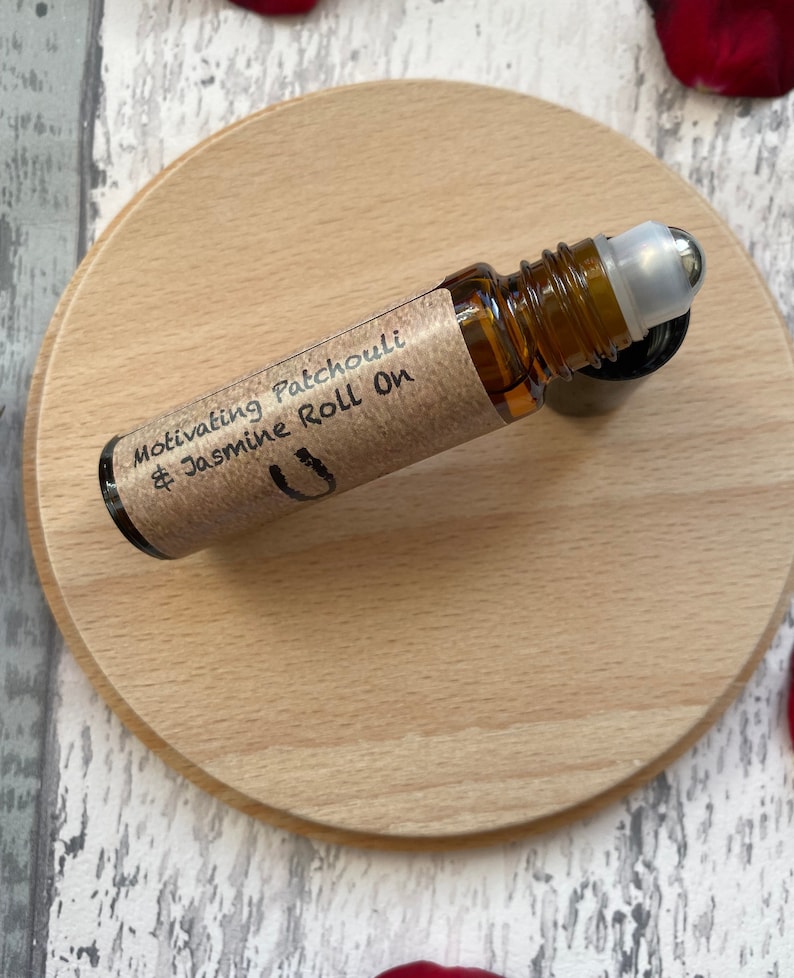 May include: A brown glass roll-on bottle with a silver roller ball. The bottle is labelled "Motivating Patchouli & Jasmine Roll On".