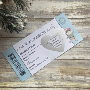 May include: A blue and white boarding pass with the text "A Magical Journey Awaits..." and "Boarding Pass:"  The pass has a silver heart-shaped sticker with the text "You are going to Lapland and seeing Santa Claus & His Reindeer."