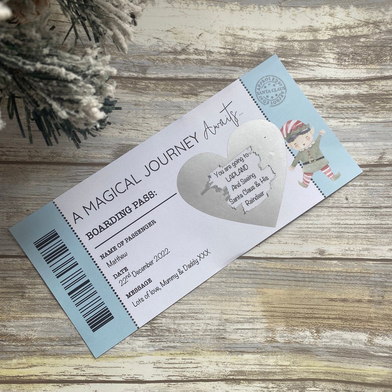 May include: A blue and white boarding pass with the text "A Magical Journey Awaits..." and "Boarding Pass:"  The pass has a silver heart-shaped sticker with the text "You are going to Lapland and seeing Santa Claus & His Reindeer."