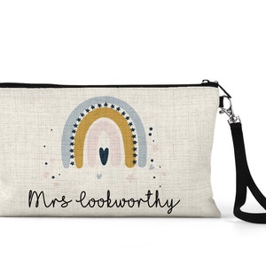 May include: A beige canvas zippered pouch with a black strap. The pouch features a colorful rainbow design with stars and a heart. The text "Mrs. Lookworthy" is printed on the front.