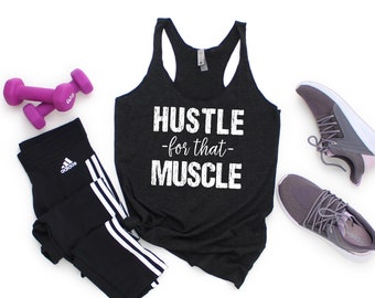 Può includere: Canotta nera con la scritta "Hustle -for that- Muscle" in bianco. La canotta è abbinata a leggings neri, manubri rosa e scarpe da ginnastica viola.