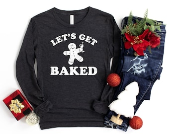 Pode incluir: Uma camisa de manga comprida cinza escura com um gráfico branco de um homem de gengibre segurando uma taça de martini. O texto "Let's Get Baked" é impresso em branco abaixo do homem de gengibre.