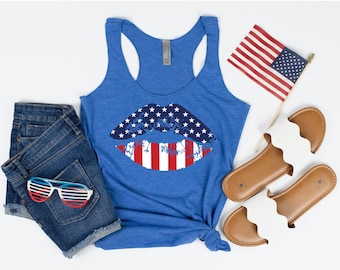 Könnte beinhalten: Ein blaues Tanktop mit einem rot-weiß-blauen Lippen-Design. Die Lippen sind in Form der amerikanischen Flagge. Das Tanktop liegt auf einem weißen Hintergrund mit einem Paar weißen Sandalen, einer blauen Jeans-Shorts und einer kleinen amerikanischen Flagge.