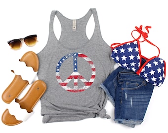 Könnte beinhalten: Ein graues Tanktop mit einem Peace-Zeichen-Motiv in Form einer abgenutzten amerikanischen Flagge. Das Tanktop wird mit Jeans-Shorts, einem Bikini-Oberteil mit Sternenmuster und einer Sonnenbrille kombiniert.
