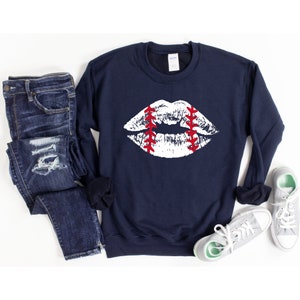 May include: A navy blue sweatshirt with a white baseball-themed lip print. The lips are outlined in red stitching.