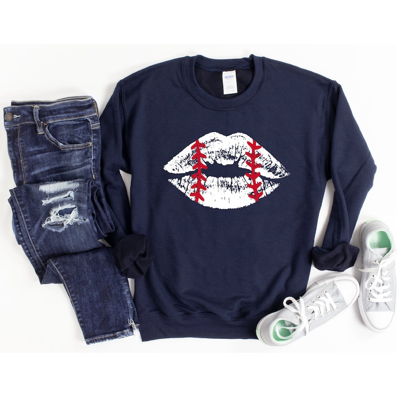 May include: A navy blue sweatshirt with a white baseball-themed lip print. The lips are outlined in red stitching.